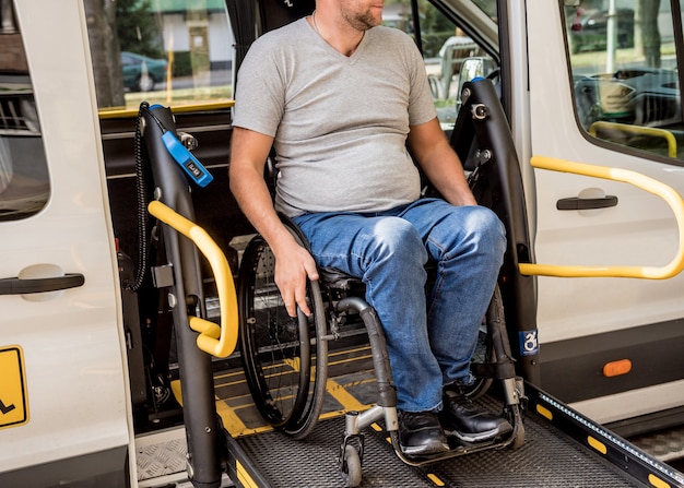 A man in a wheelchair on a lift of a specialized vehicle for\
people with disabilities.