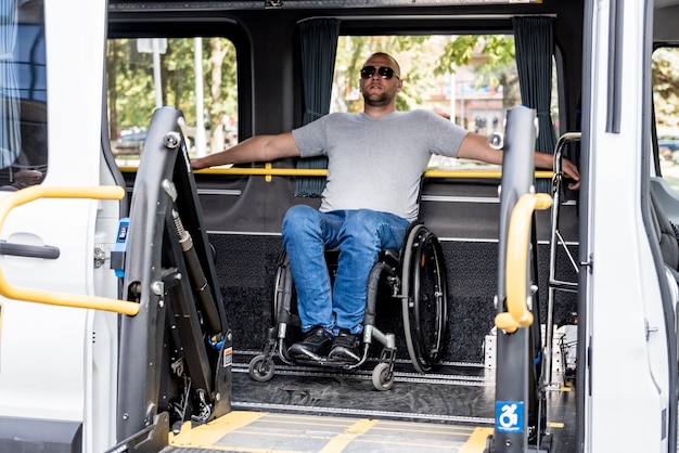 A man in a wheelchair on a lift of a vehicle for people with\
disabilities