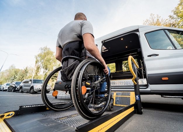 Foto un uomo su una sedia a rotelle si sposta verso l'ascensore di un veicolo specializzato per persone con disabilità.