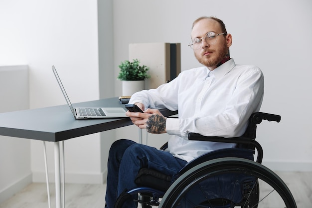 A man wheelchair in the office works at a laptop with a phone working online social networks and startup integration into society the concept working person with disabilities real person closeup