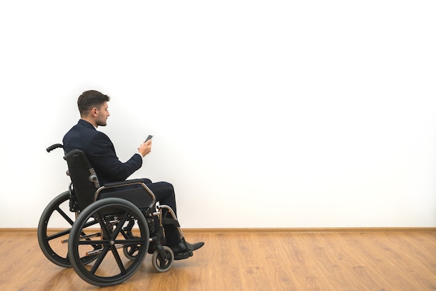 The man in a wheelchair phones on the white wall background