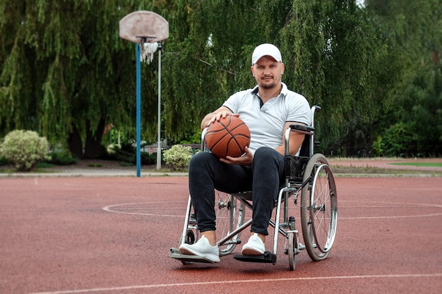 A man in a wheelchair plays basketball on the sports ground. The concept of a disabled person, a fulfilling life, a person with a disability, fitness, activity, cheerfulness.