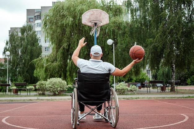 휠체어를 탄 남자가 운동장에서 농구를 하고 있습니다. 장애인, 만족스러운 삶, 장애가 있는 사람, 건강, 활동, 쾌활함의 개념.
