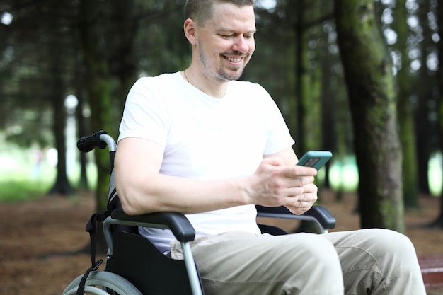 Man in wheelchair sits holding smartphone in his hand and smile