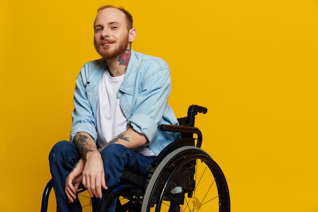 A man in a wheelchair smile and happiness thumb up with tattoos on his hands sits on a yellow studio background the concept of health a person with disabilities