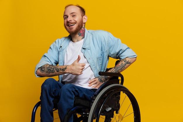 A man in a wheelchair smile and happiness thumb up with tattoos on his hands sits on a yellow studio background the concept of health a person with disabilities