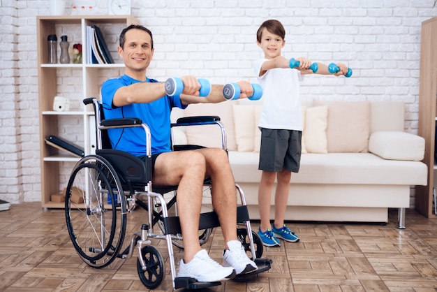 車椅子と手の中にダンベルを持つ息子の男。