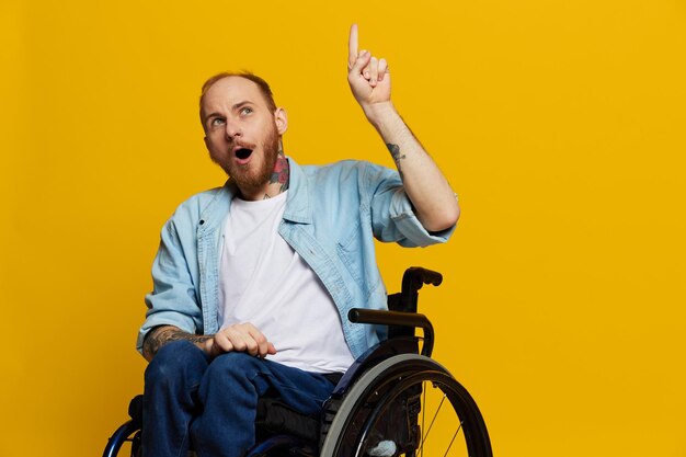 A man in a wheelchair surprised with tattoos on his arms sits on a yellow studio background the person