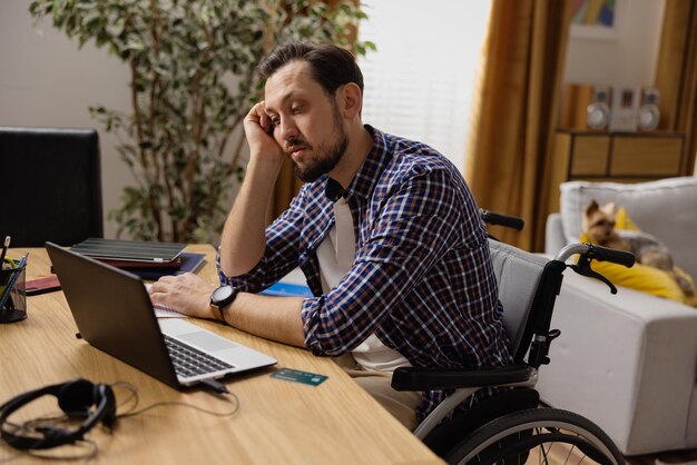 A man in a wheelchair tired of working props his head with his hand looking boredly