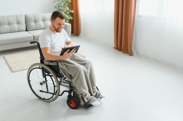 Man in wheelchair using tablet computer at home Positive retired male with physical disability browsing web on touch pad watching video online indoors