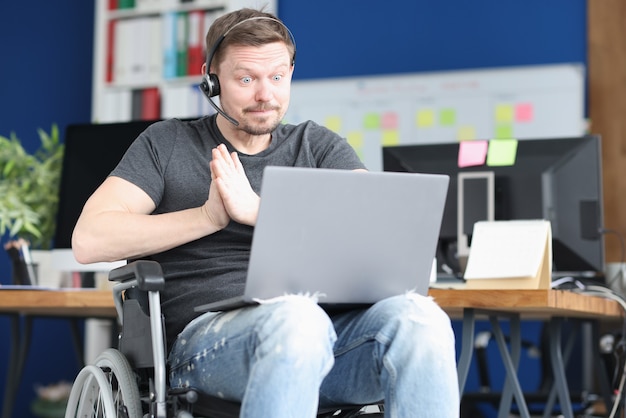 Man in wheelchair and wearing headphones with microphone works on laptop