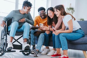 Man on wheelchair with friends having fun watching smart mobile phone device