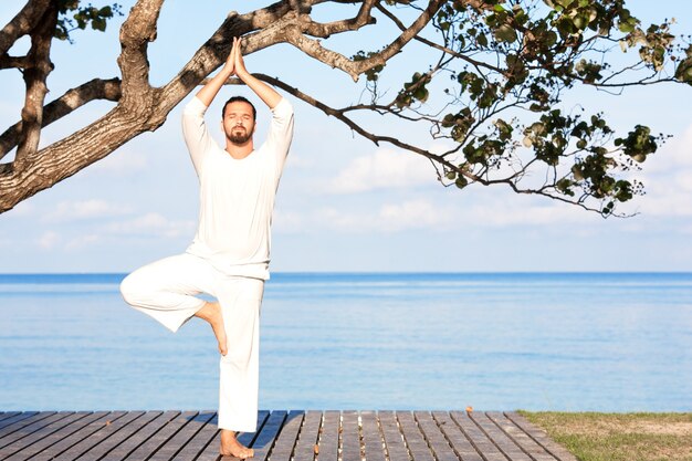 木製の桟橋でヨガを瞑想する白い服を着た男