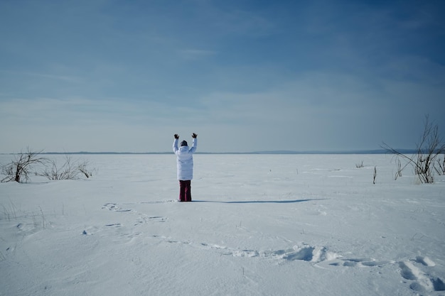 A man in a white coat stands on a frozen lake with his arms up in the air.