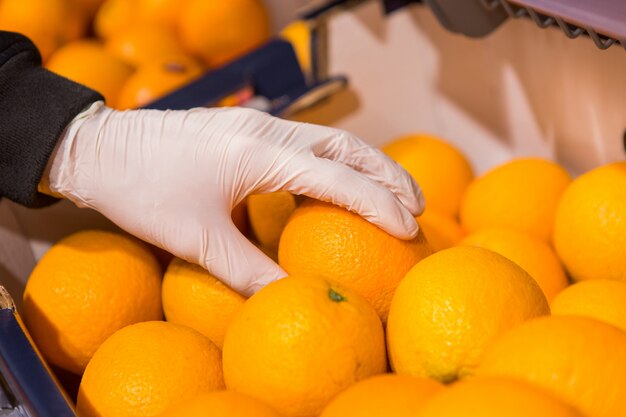 A man in white gloves in a store buys food. Man holds an orange in his hands