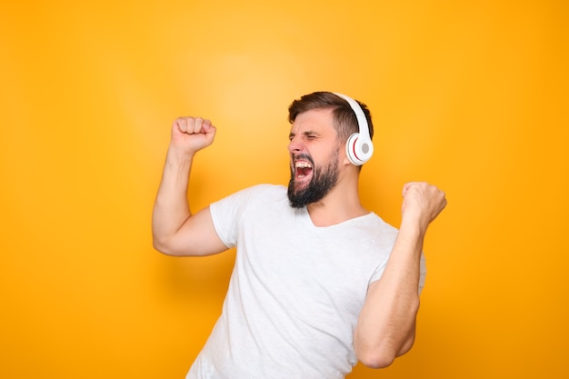 A man in white headphones listens to music and sings loudly, raising his hands up.