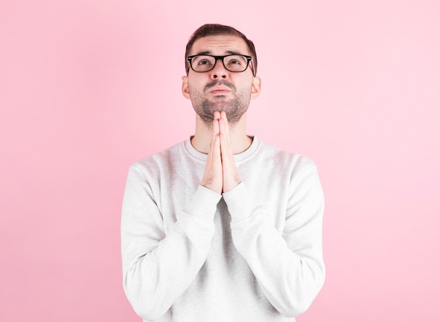 Man in a white home sweater makes a wish for his birthday over pink wall.