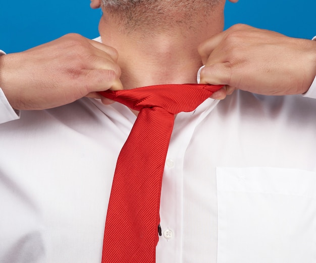 Man in a white office shirt tears off a red satin tie from his\
neck