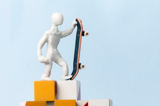 A man in white plasticine is standing on top of cubes on a blue background and holding a skateboard in one hand. concept of motivation, success, achievement of the set goal.
