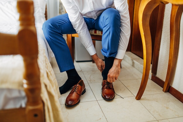 Foto l'uomo con una camicia bianca e pantaloni blu si sta allacciando le scarpe seduto su una sedia primo piano