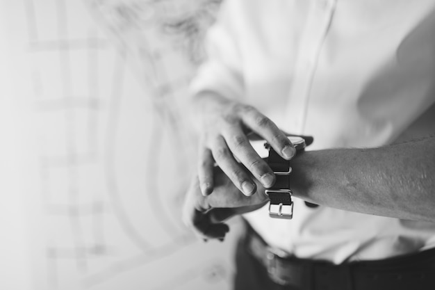 Man in a white shirt fastens a wristwatch on his hand closeup black and white photo