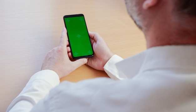 man in a white shirt holding a black mobile phone with a blank green screen