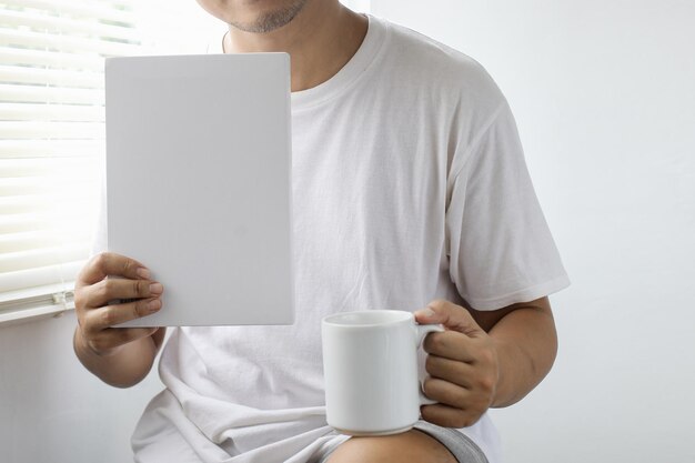 Man in white shirt holding white book and white glass Mock up of mug and book