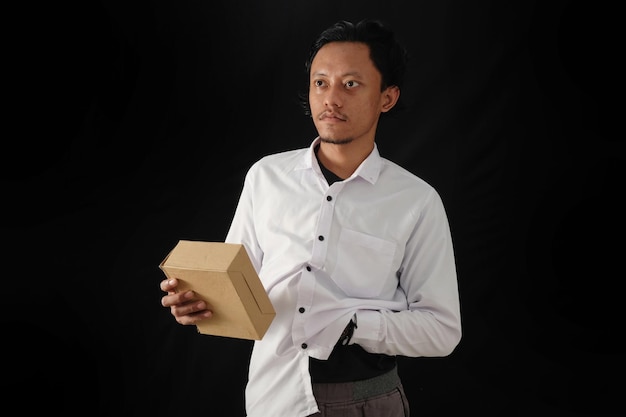 A man in a white shirt holds a brown box in front of a black background.