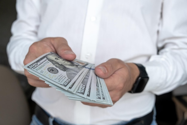 A man in a white shirt holds money counts it and offers it to another