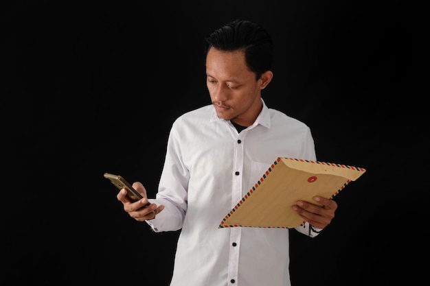 A man in a white shirt holds a phone and looks at a mailbox.