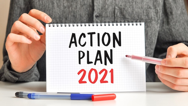 A man in a white shirt holds a piece of paper with the text: ACTION PLAN 2021