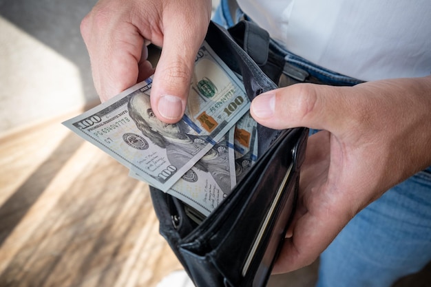 A man in a white shirt holds a wallet with money counts it and offers it to another