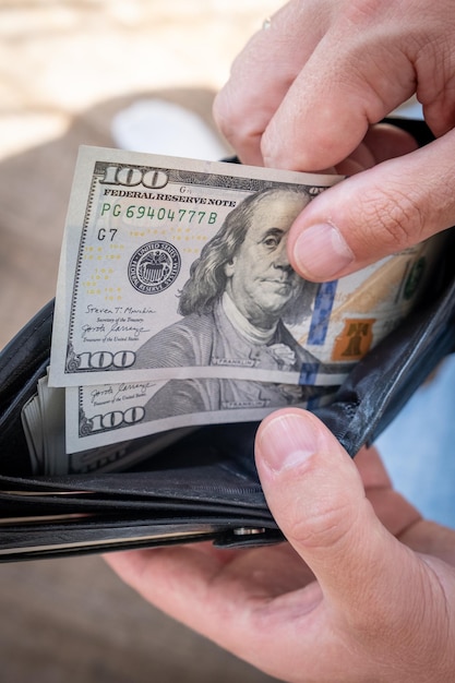 A man in a white shirt holds a wallet with money counts it and offers it to another