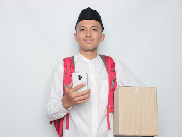 A man in a white shirt is holding a box and a phone