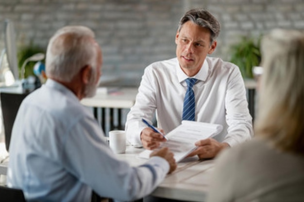 a man in a white shirt is signing a contract with a man in a suit and tie