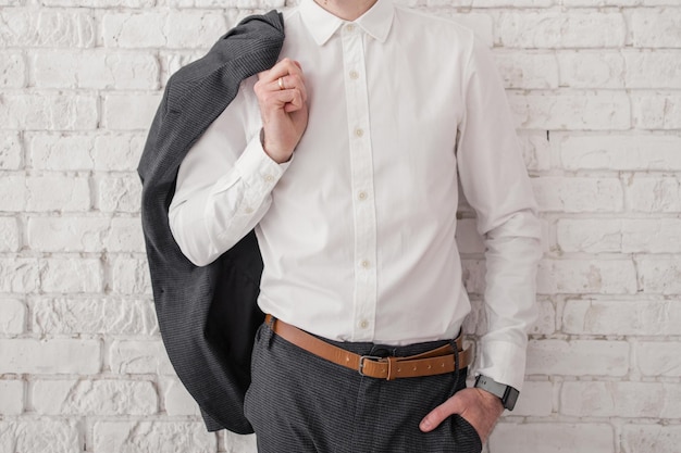 A man in a white shirt and jacket near a brick wall