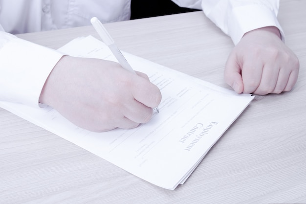 Foto un uomo in camicia bianca si siede a un tavolo e firma un contratto di lavoro