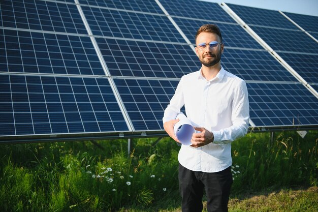 Man in white shirt standing near photovoltaic panels on sunny day in countryside