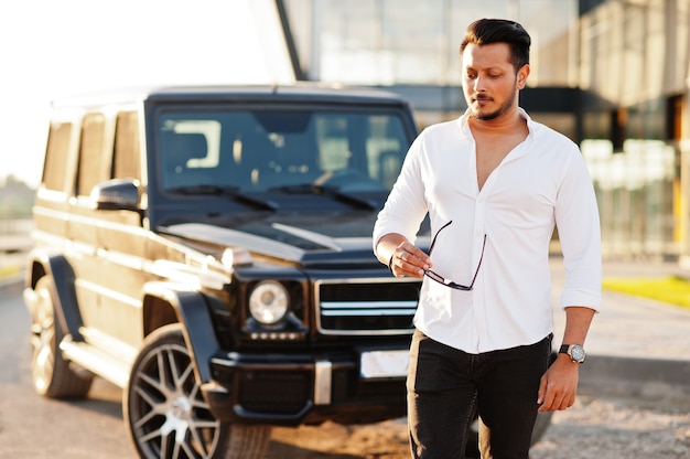 Man in white shirt and sunglasses posing near black suv car