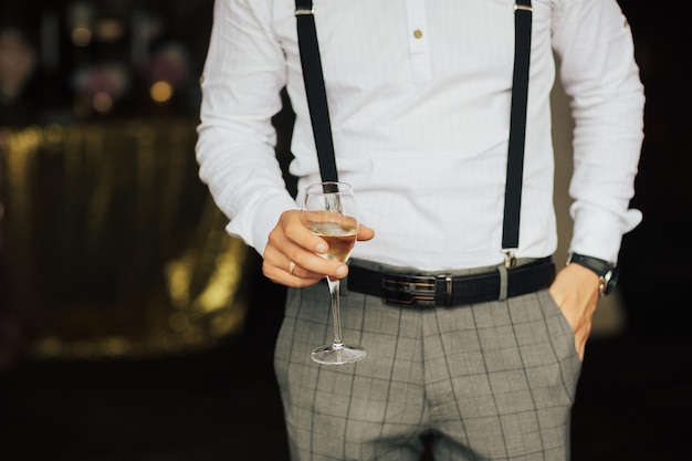 man in white shirt suspenders and classical trousers holding glass of champagne