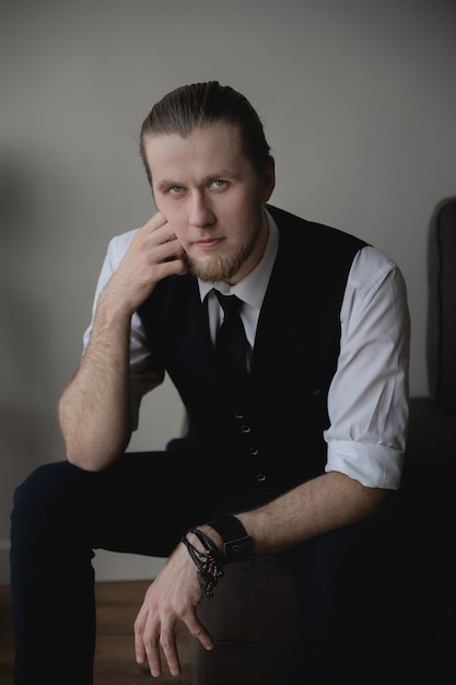 man in a white shirt and vest sits on an armchair and poses