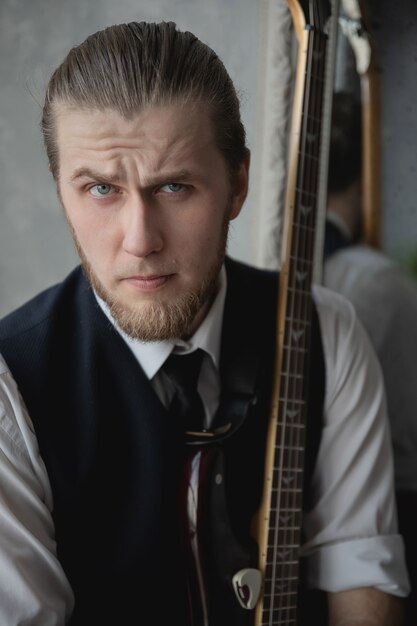 man in a white shirt and vest sits on a sofa with a guitar