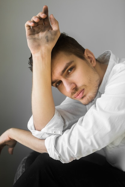 Man in white shirt with dirty face on gray background. Sitting worker. Hard work