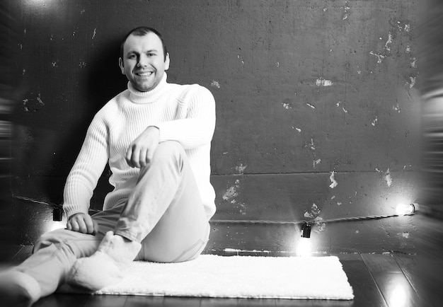 A man in a white sweater in a dark room listening to music