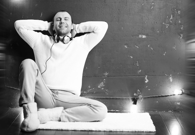 A man in a white sweater in a dark room listening to music