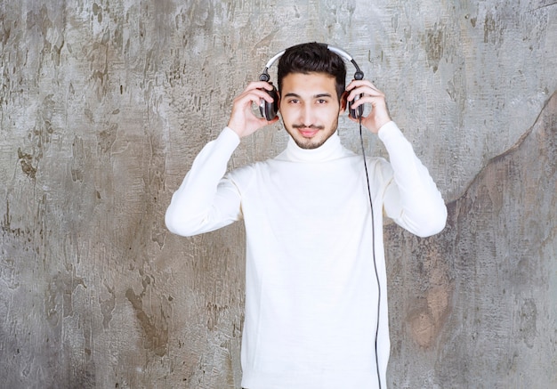 Man in white sweater wearing headphones and listening the music.