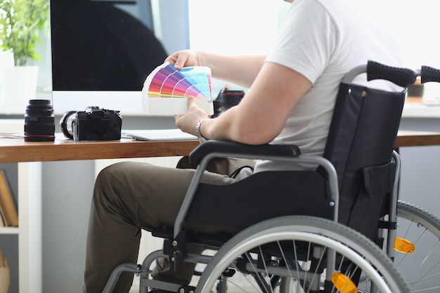 Man in white T-shirt and green pant sit in wheelchair and hold multi-colored palette in his hand.