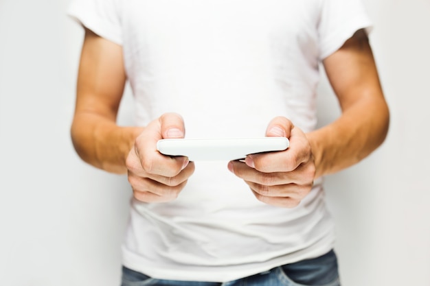 Человек в белой футболке с помощью мобильного смартфона, белая стена на поверхности