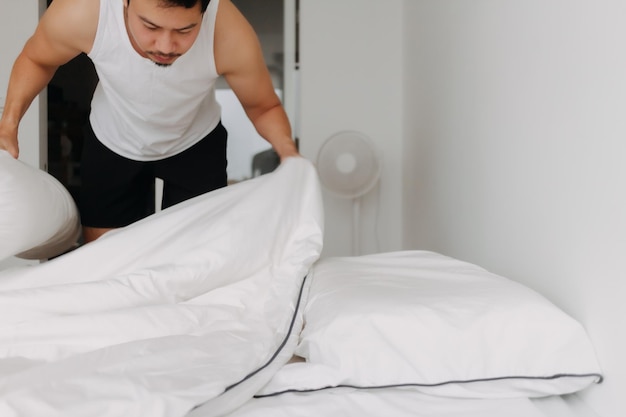 Man in white tank top is making bed folding into a sofa