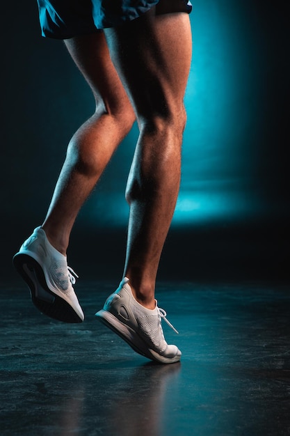 Man in white training shoes and shorts doing exercises against the blue light background and hopping